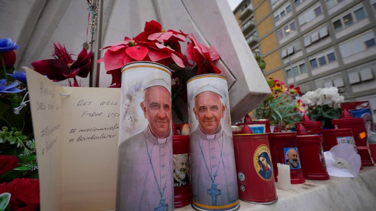 Candles with the pictures of Pope Francis are seen under the statue of late Pope John Paul II, outside Agostino Gemelli Polyclinic in Rome, Wednesday, Feb. 19, 2025, where the Pontiff is hospitalized since Friday, Feb. 14. (AP Photo/Andrew Medichini)