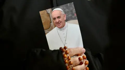 EPA In a close-up image of her hands, a nun clutches an image of the Pope and rosary beads