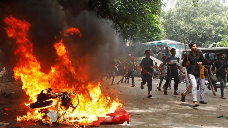 People run past a vehicle set on fire by protesters during a rally against Ms Hasina.  Pic: Reuters/Rajib Dhar