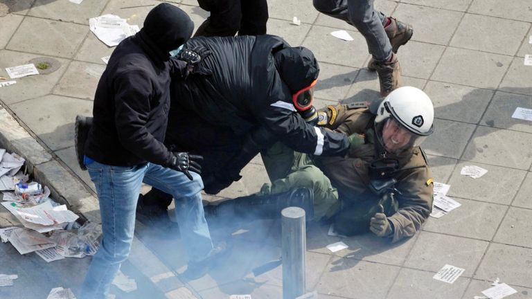 Hooded protesters beat a riot policeman after a massive rally in central Athens, Greece to mark two years since a deadly rail disaster that has also triggered hundreds of other demonstrations and a general strike, on Friday, Feb. 28, 2025. (AP Photo/Thanassis Stavrakis)