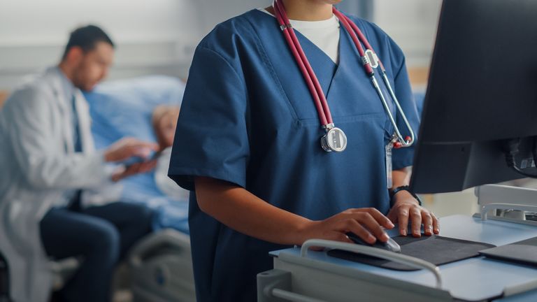 Hospital Ward: Professional Smiling Black Female Head Nurse or Doctor Wearing Stethoscope Uses Medical Computer. In the Background Patients in Beds Recovering Successfully after Sickness and Surgery