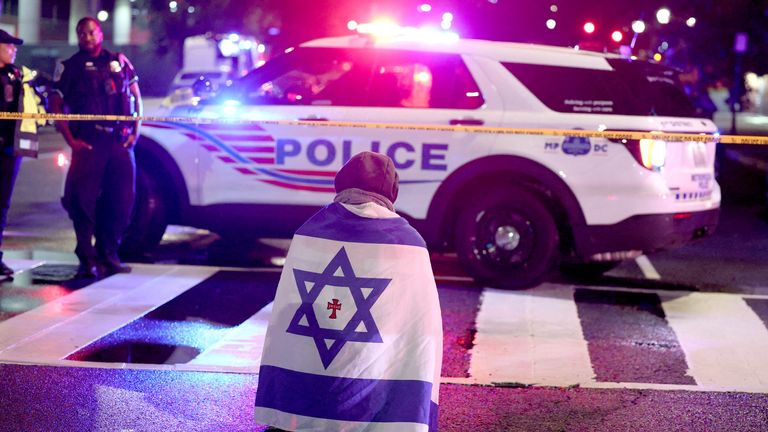 A man with an Israeli flag kneels at the scene.  Pic: Reuters